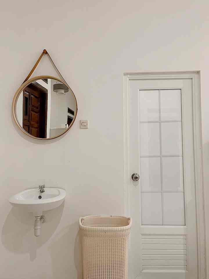 White and natural tone bathroom entrance area featuring a round mirror, sink, and bathroom door with a clean atmosphere