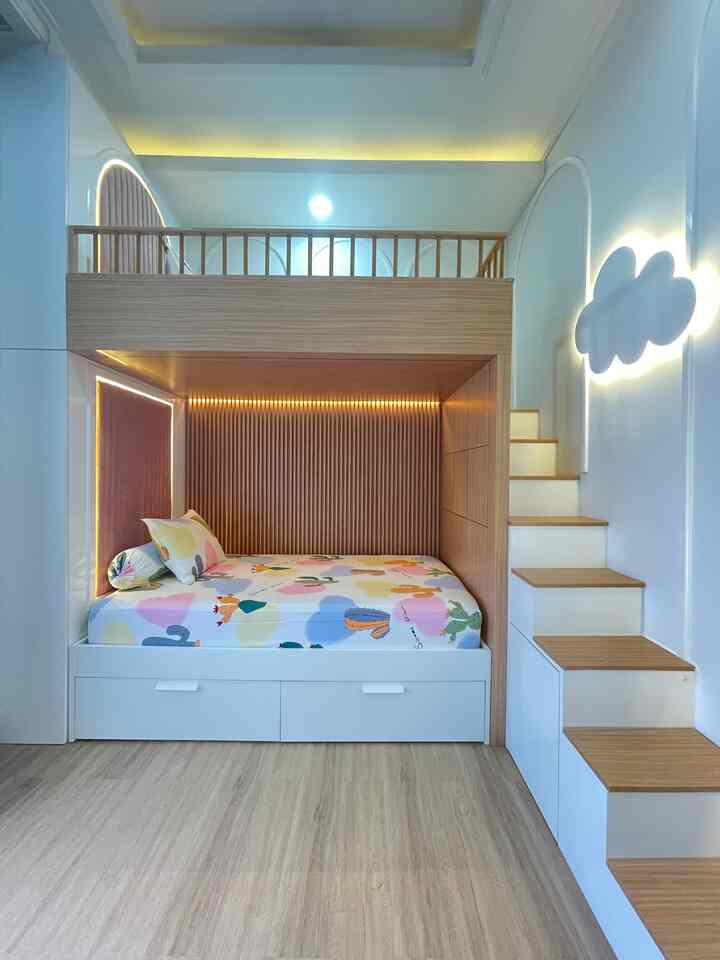 Design kamar anak yang simple dan tidak terlalu banyak barang, akan membuat kamar terlihat rapi dan nyaman.  Kisi-kisi/ wall panel pada sisi tempat tidur, menjadi focal point di kamar anak ini. 
Barang-barang yang ada di kamar anak antara lain: 
1. Tempat tidur dibuat bersusun/ bertingkat untuk menghemat tempat. 
2. Tangga sekaligus storage/ penyimpanan barang.
3. Lemari pakaian
4. Meja belajar 
5. Lampu awan sebagai lampu tidur sekaligus sebagai wallart

Material yang digunakan untuk furniture adalah multiplek dengan finishing HPL. Dengan perpaduan warna putih dan kayu. 

Tips menjaga kamar anak agar terlihat rapi, menarik dan nyaman :
1. Perbanyak tempat penyimpanan/ storage
Karena anak-anak cenderung mengumpulkan barang yang dapat membuat kamar berantakan, seperti buku dan mainan. Nah, memiliki banyak storage/ tempat penyimpanan adalah “kunci”. Di kamar anak ini, bunkbed menggunakan tangga sekaligus sebagai storage / tempat penyimpanan. Laci di bawah tempat tidur dan headboard juga kami jadikan storage penyimpanan, untuk menyimpan mainan, pakaian dan buku, sehingga tidak ada alasan kamar berantakan.
2. Pemilihan tempat tidur Untuk pemakaian jangka panjang
Karena plafon cukup tinggi, maka tempat tidur anak dibuat bersusun/ bertingkat (bunkbed). Sehingga menghemat tempat untuk ukuran kamar yang tidak terlalu luas. 
3. Pilih warna yang disukai anak
Sebisa mungkin pilih warna yang soft atau tidak mencolok. Bisa memilih warna monokrom atau netral, tapi pastikan memberikan banyak aksen warna yang bervariasi sebagai dekorasi agar kamar anak lebih ceria. 
4. Ruang Bermain
Pastikan kamar anak kuga bisa menjadi tempat bermain anak. Ini adalah cara agar anak nyaman di rumah, terutama di kamarnya. 
5. Berikan anak tanggung jawab untuk menjaga kebersihan dan kerapihan kamarnya. Setiap selesai bermain, anak-anak selalu diajarkan untuk meletakkan barang/ mainan di tempatnya masing-masing.

#DekorasiKamarAnak #InspirasiKamarAnak #KidsRoomStyling


