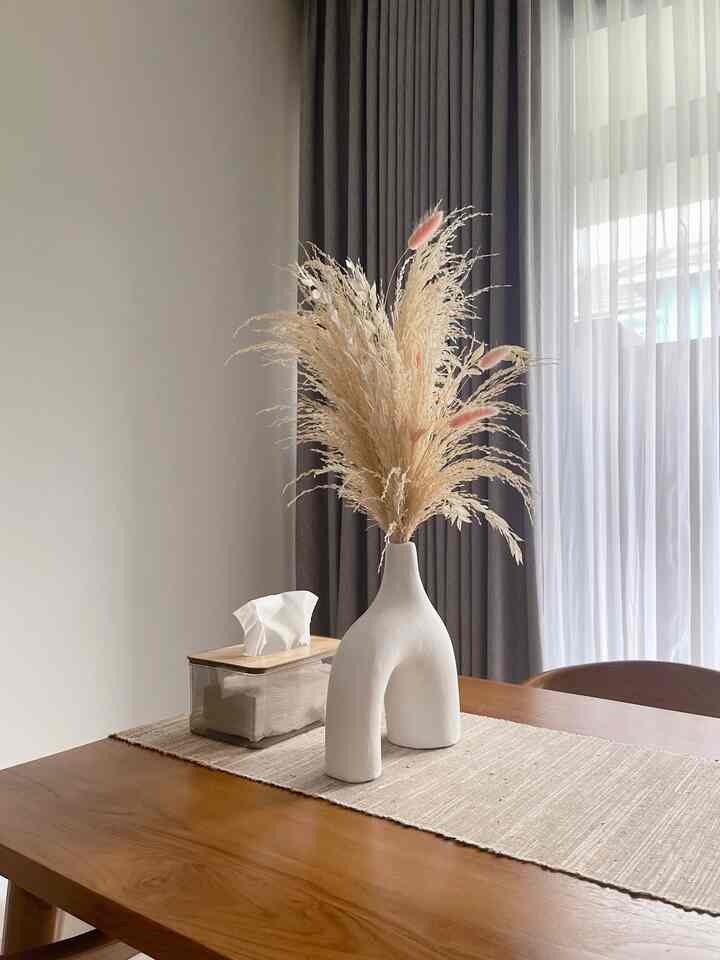 Natural color dining room featuring a wooden dining table with a uniquely designed white vase and table runner, creating a cozy atmosphere