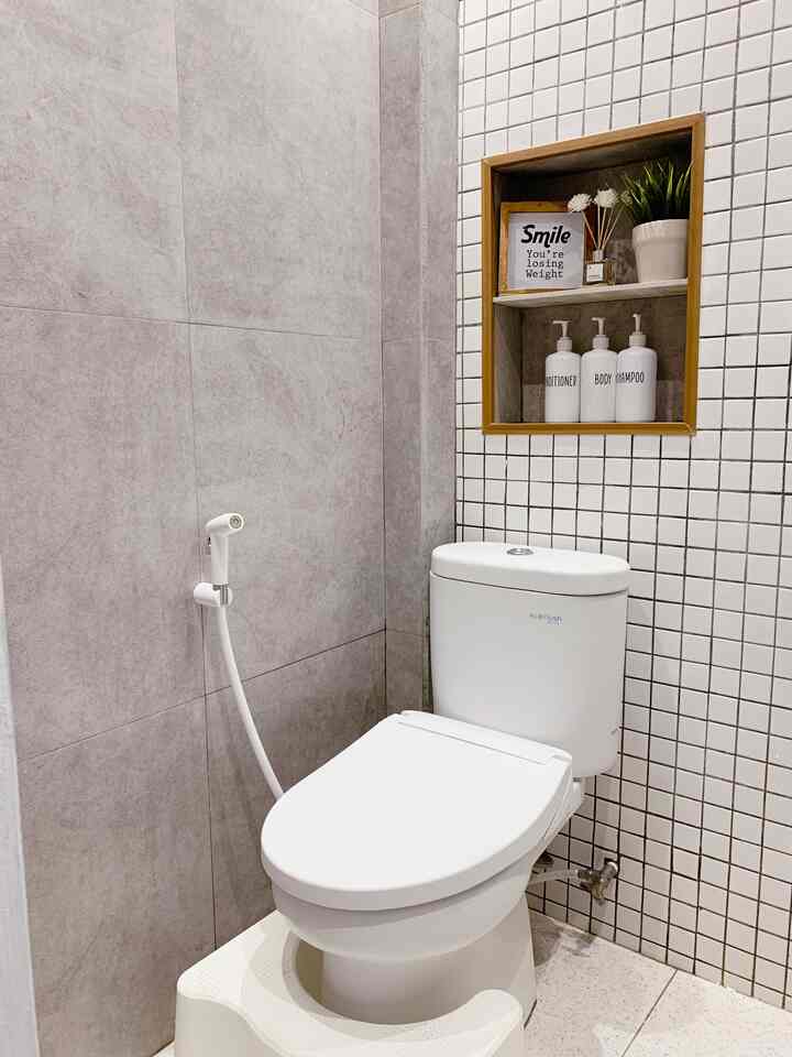 Compact bathroom in white and gray tones featuring a centrally placed toilet and wooden frame shelf with minimalistic feel
