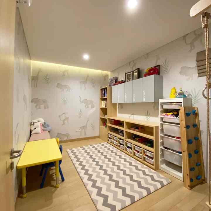 Natural-tone kids' room featuring wood floor, white storage cabinets, a yellow desk, and a gray zigzag patterned carpet creating a cozy play area
