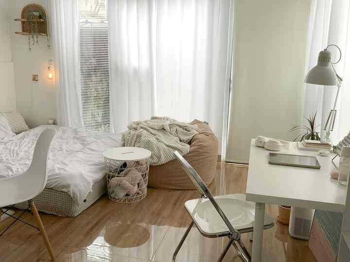 Bright white and beige toned bedroom featuring a home office setup and a bean bag with a simple, natural atmosphere