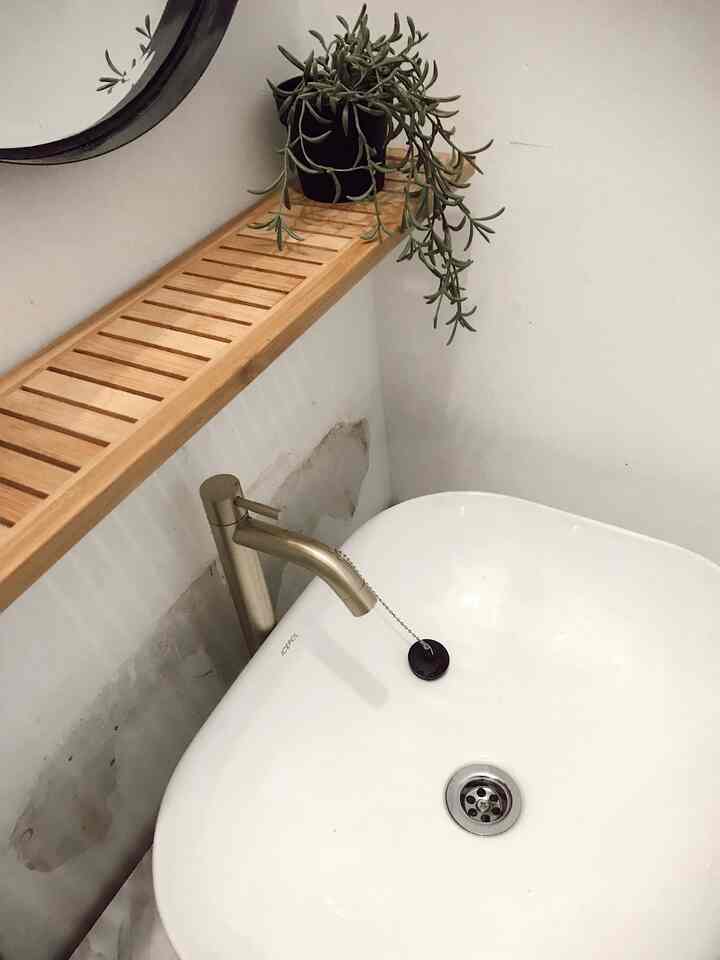 A simple modern bathroom with white walls and sink featuring a brown wooden rack above, creating a natural and clean look