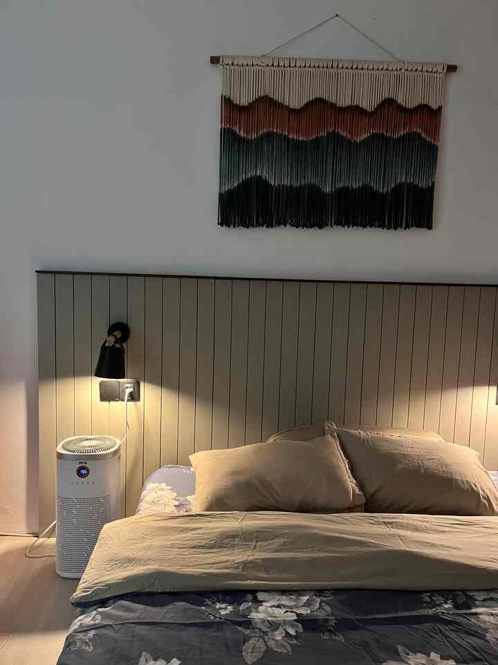 Beige-toned bedroom featuring bed, nightstand, wall sconces, and air purifier creating a cozy and natural atmosphere