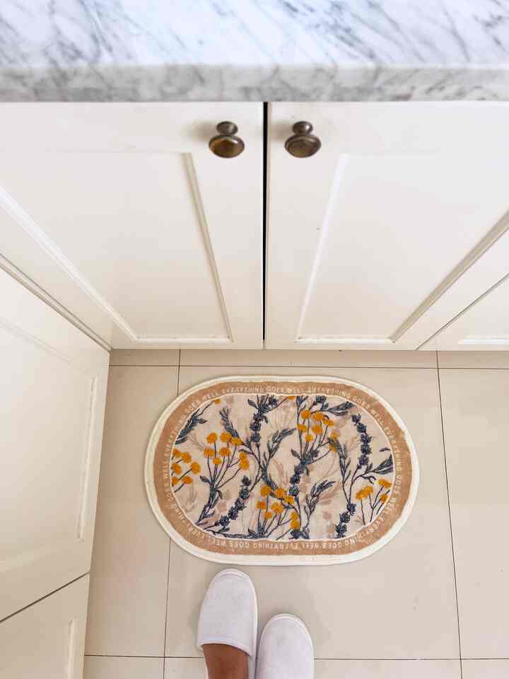 White-toned kitchen space featuring white cabinets and a beige bath mat with yellow floral patterns, creating a clean and cozy atmosphere