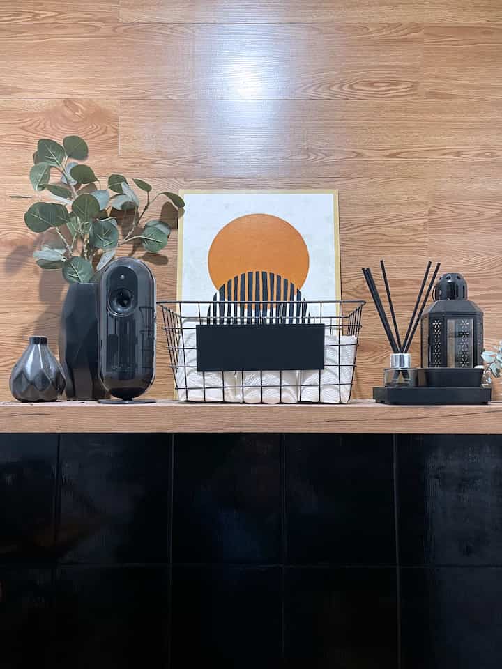 Black and white bathroom shelf with warm wood tones, neatly arranged towels and diffuser creating a minimalist atmosphere