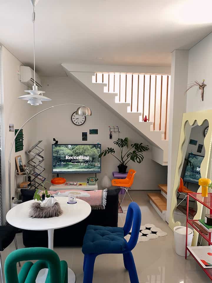 Bright white and natural wood tone small living room featuring colorful chairs, sofa, and large mirror with cozy atmosphere