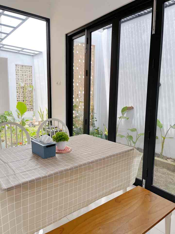 Bright open balcony dining space featuring beige checkered tablecloth and white chairs with garden views