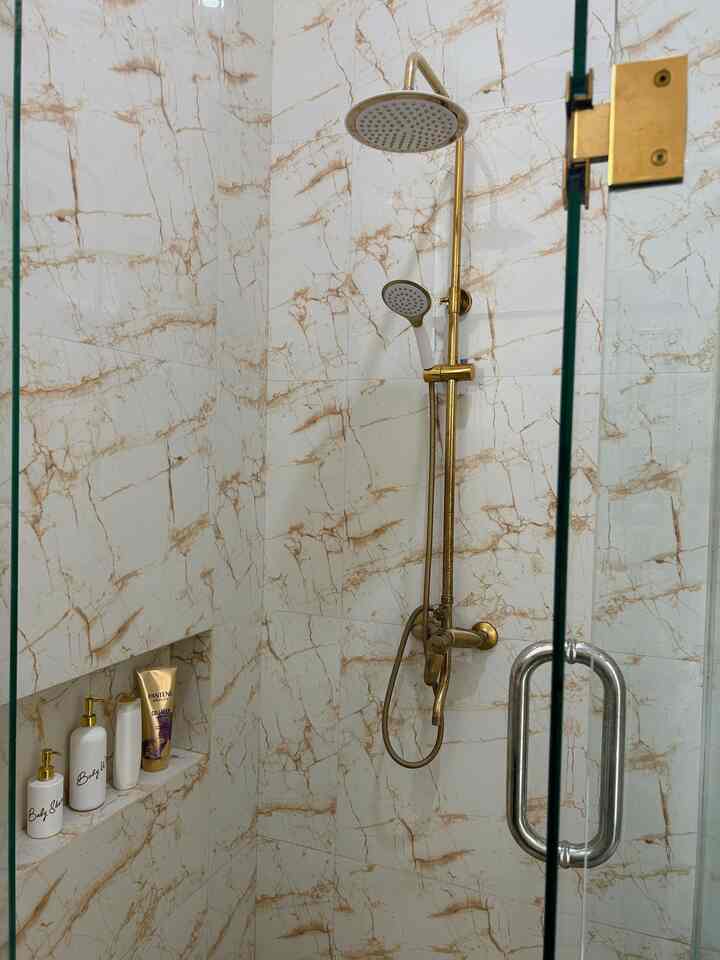 Gold-toned bathroom shower booth featuring marble tiles and golden shower fixtures with an elegant atmosphere