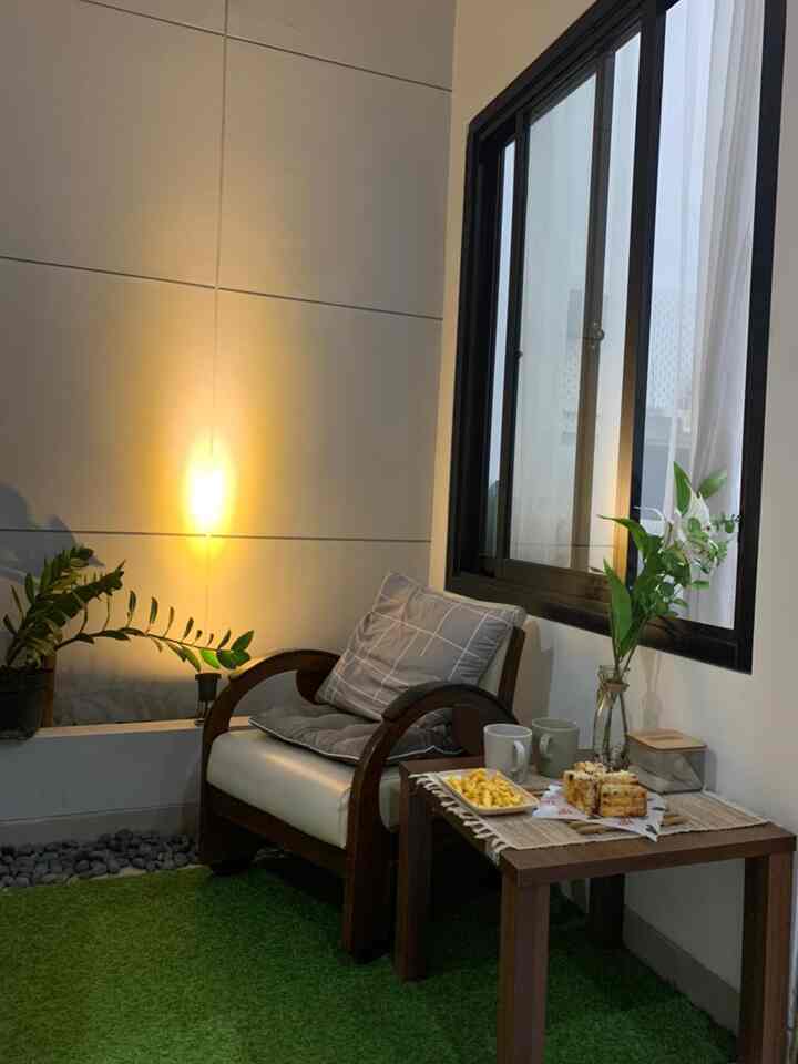 Small natural-toned living space with warm lighting, plants, and wooden armchair and table creating cozy atmosphere