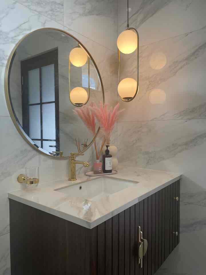 White and brown tone bathroom featuring a modern classic sink area with gold accent round mirror and pendant light