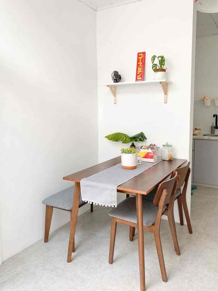 White-walled dining room with wood tone table set for three, featuring simple natural plant decor and bright atmosphere