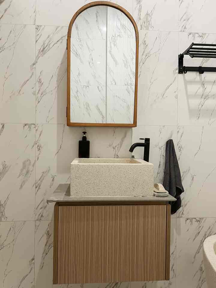 A white and natural-toned bathroom featuring a wooden framed mirror and a natural stone sink with a clean aesthetic
