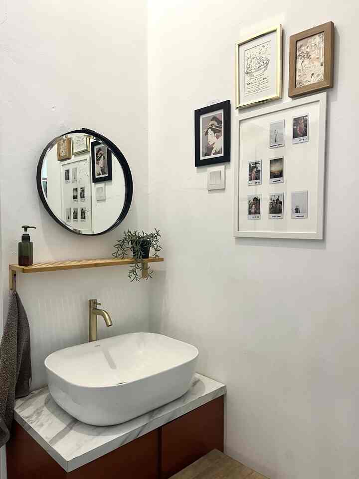 Small bathroom corner with white walls and wood-tone cabinet, featuring round mirror and picture frames in a simple setting