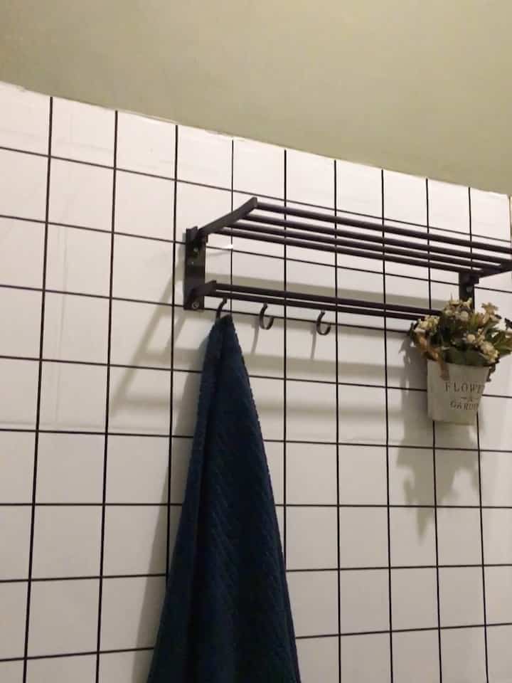 Minimal bathroom with light green wall and white tiled walls, featuring black towel rack holding a dark blue towel