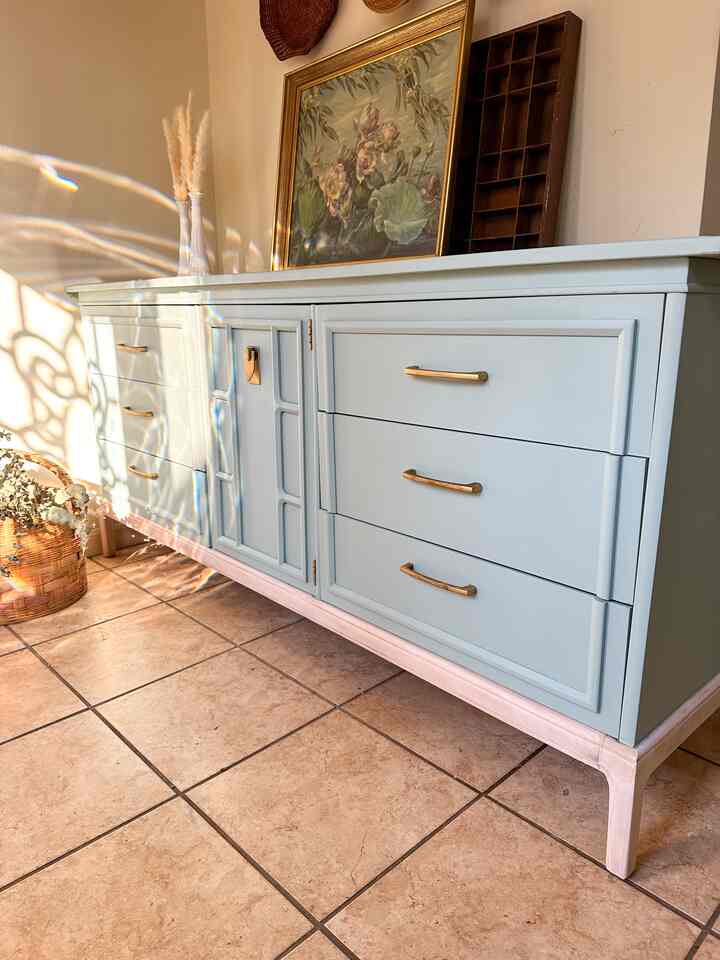 A natural bohemian space featuring a pale blue storage cabinet, warm brown tiled floor, and a floral watercolor painting as focal points