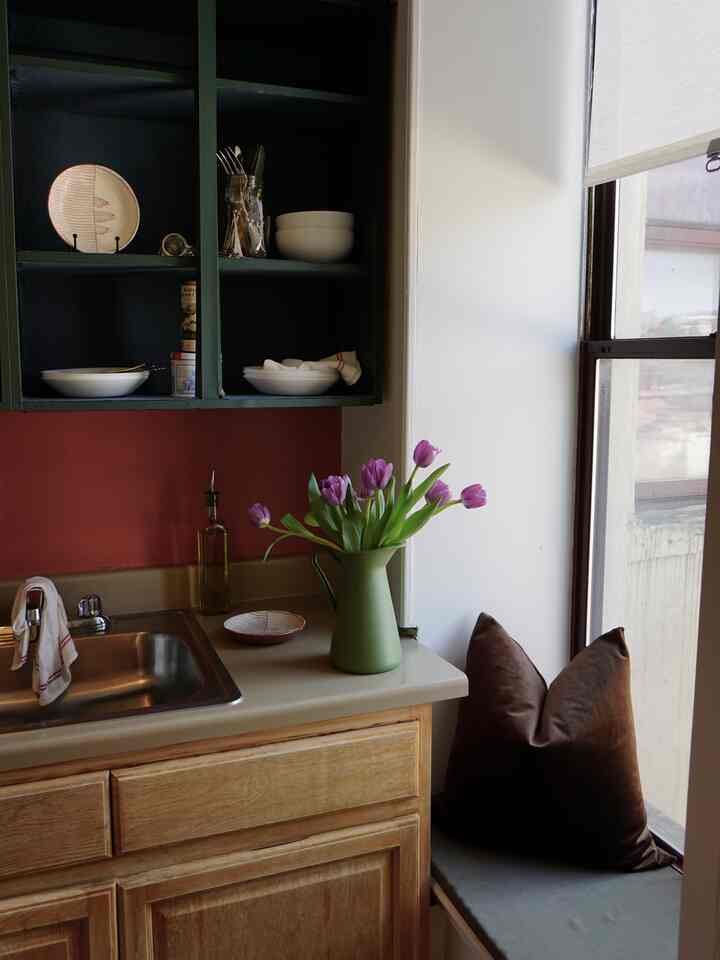 Cozy apartment kitchen in warm brown and natural tones featuring a window seat and green vase with tulips