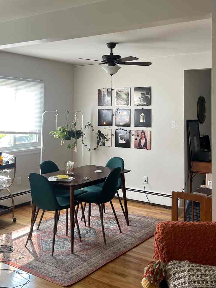 White-walled mid-century modern dining room with wood tone flooring, green dining chairs, wooden dining table, and vinyl records displayed on wall