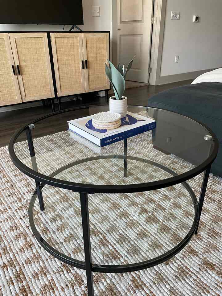 Natural-toned living room featuring a round transparent glass coffee table with a book and an artificial plant, creating a cozy arranged space