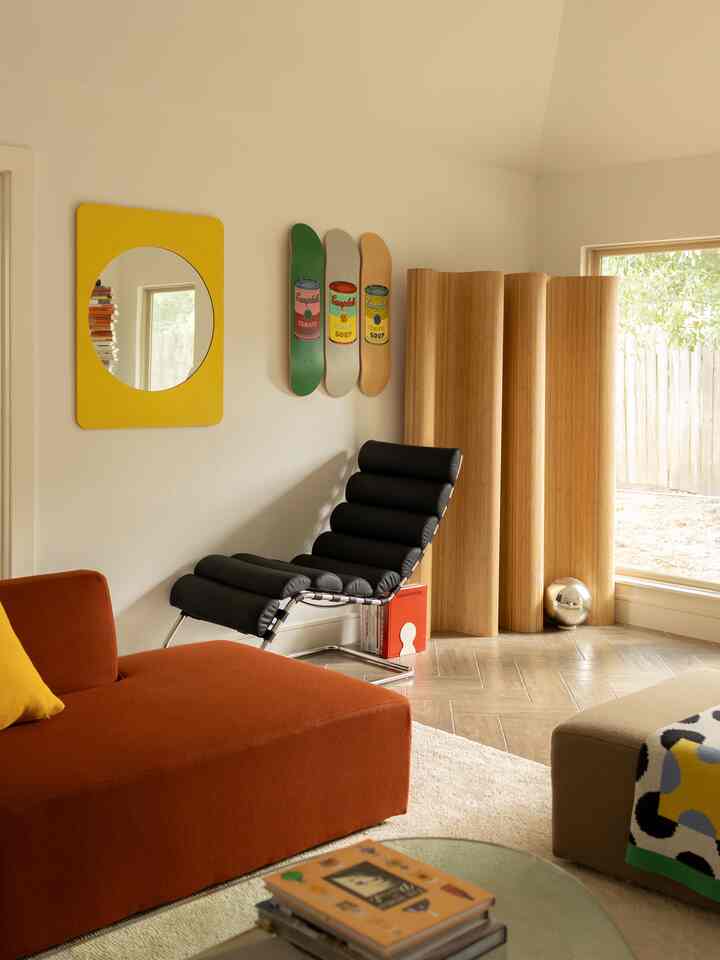 A warm orange and wood-toned living room featuring a black armchair and yellow mirror in a contemporary home gallery setting