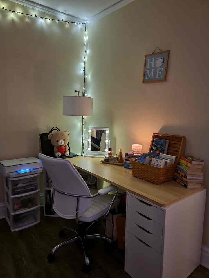 White and light brown toned home office featuring a vanity mirror, book basket, string lights, and candle creating a cozy atmosphere