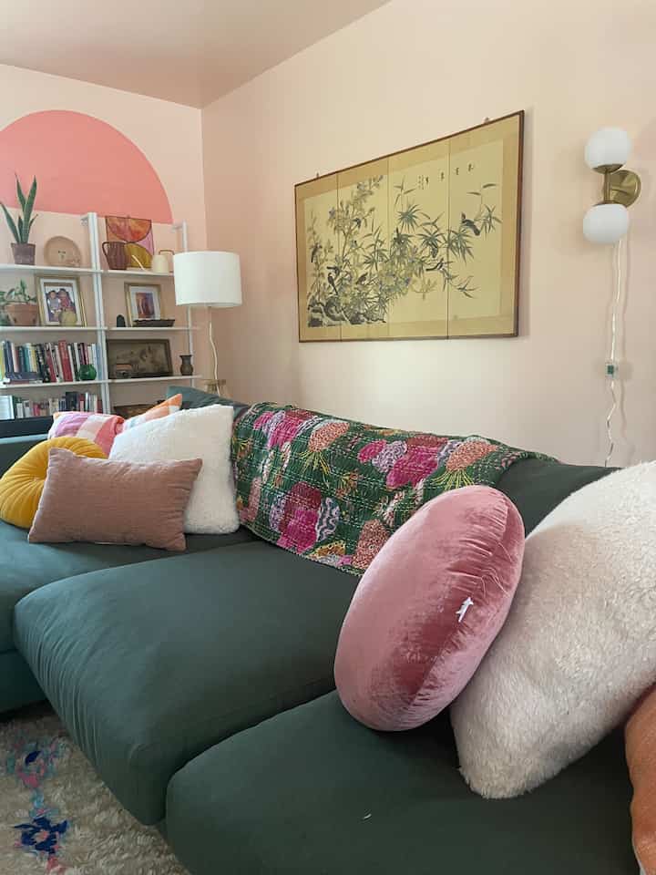 A cozy living room with pink arched wall, green sofa, and assorted cushions