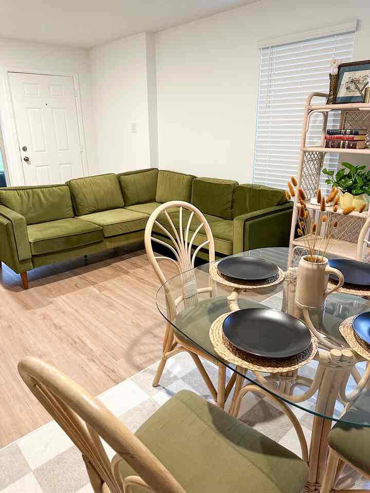 Living room in natural tones featuring an olive green sectional sofa and rattan dining chairs with a glass table