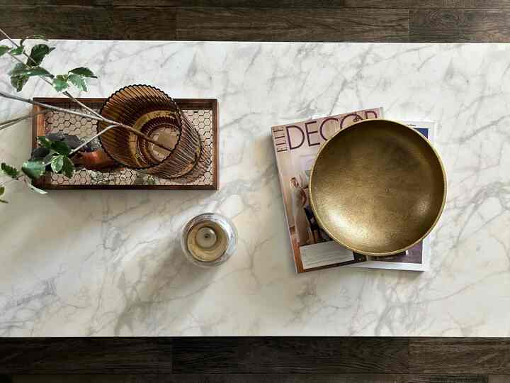 White marble top coffee table featuring gold bowl and wood tone tray with a simple, natural living room vibe