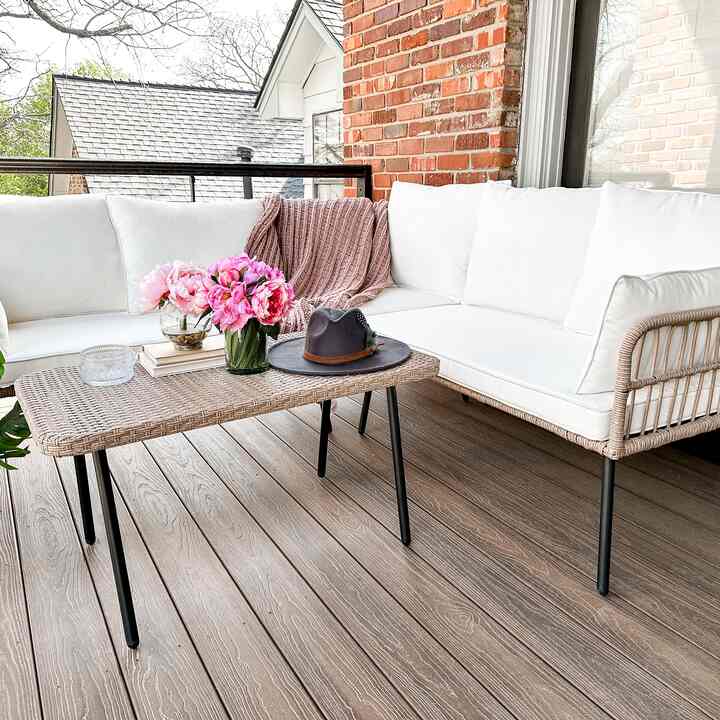 White and wood tone balcony featuring white cushioned sofa, wicker coffee table, and pink flower vases creating a natural atmosphere