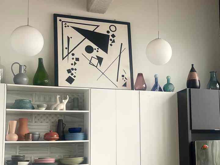 White and green toned kitchen with shelves displaying plates and bowls, featuring abstract art and pendant lights in modern natural style