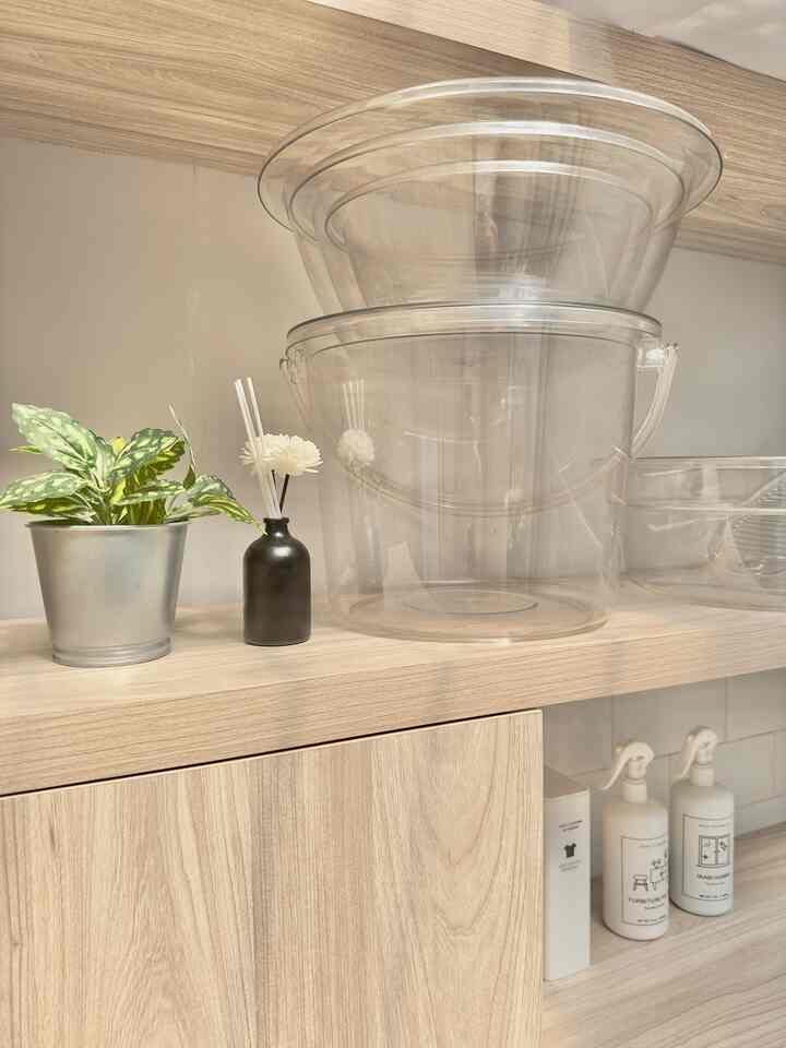 Light wood tone long and narrow compact laundry room featuring custom cabinets and transparent laundry supplies neatly arranged