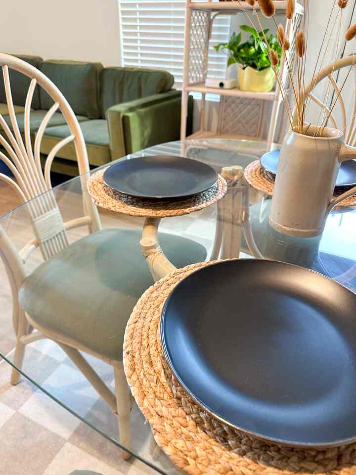 Natural wood tones and green colors blend in a living room dining area with a glass dining table and rattan chairs, creating a cozy vintage vibe