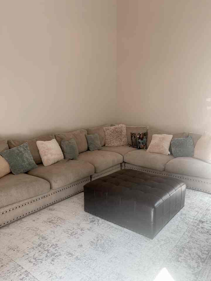 Light gray-walled living room for a 4-person family featuring a large brown leather ottoman and beige sectional sofa in a simple cozy setting