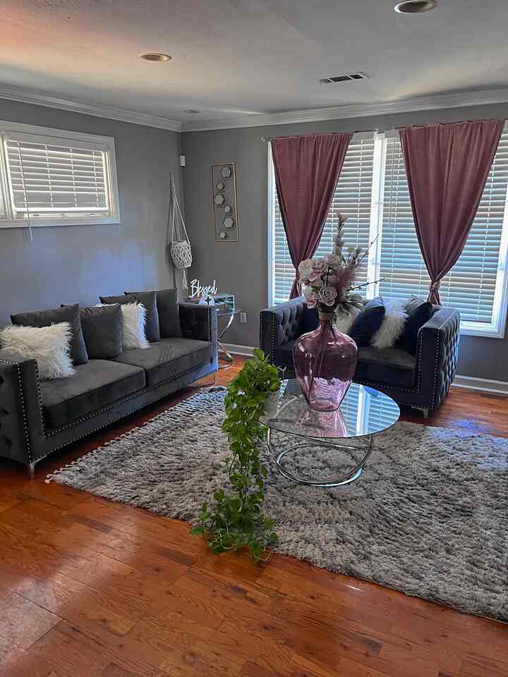 Living room with gray walls and sofas, brown wooden floor, pink curtains, and glass coffee table