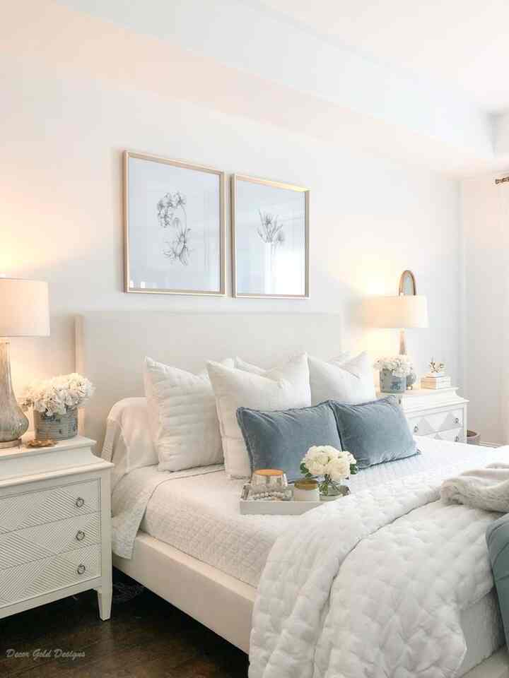 White-toned bedroom featuring a central bed flanked by nightstands, minimalist floral framed prints on the wall creating a cozy atmosphere