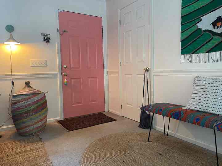 Cozy entrance with light brown flooring, white walls, a pink door, and a colorful patterned bench