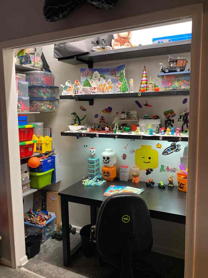 Bright white-walled small kids' workspace featuring black desk and shelves with colorful toys and organized storage containers