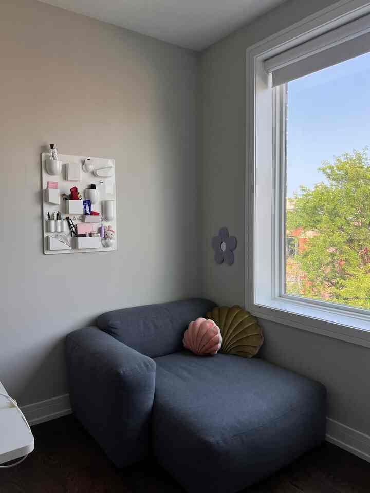 Soft gray-toned home office corner with a large window beside a comfortable gray sofa and wall-mounted organizer creating a cozy space