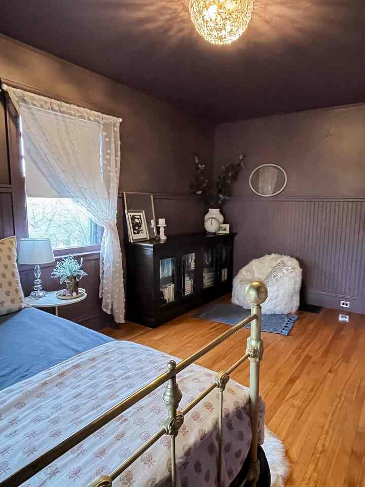 Moody bedroom with warm wood tone floor and deep purple walls, featuring a brass bed frame and white bean bag chair
