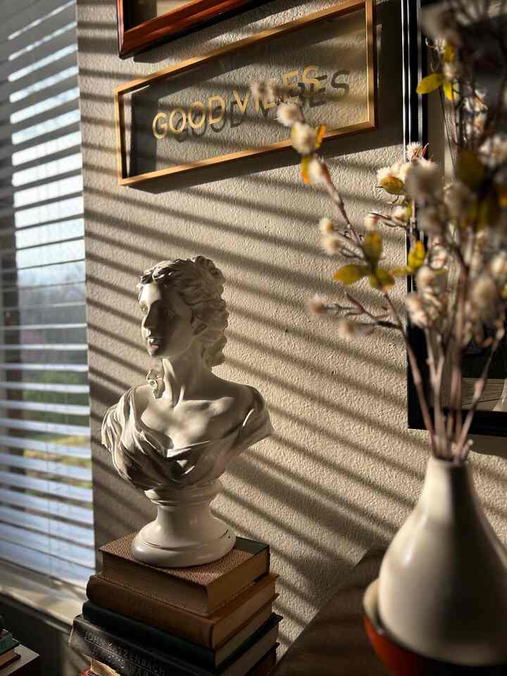 Warm afternoon sunlight illuminates a classic vintage living room corner featuring a Roman female bust and wall art