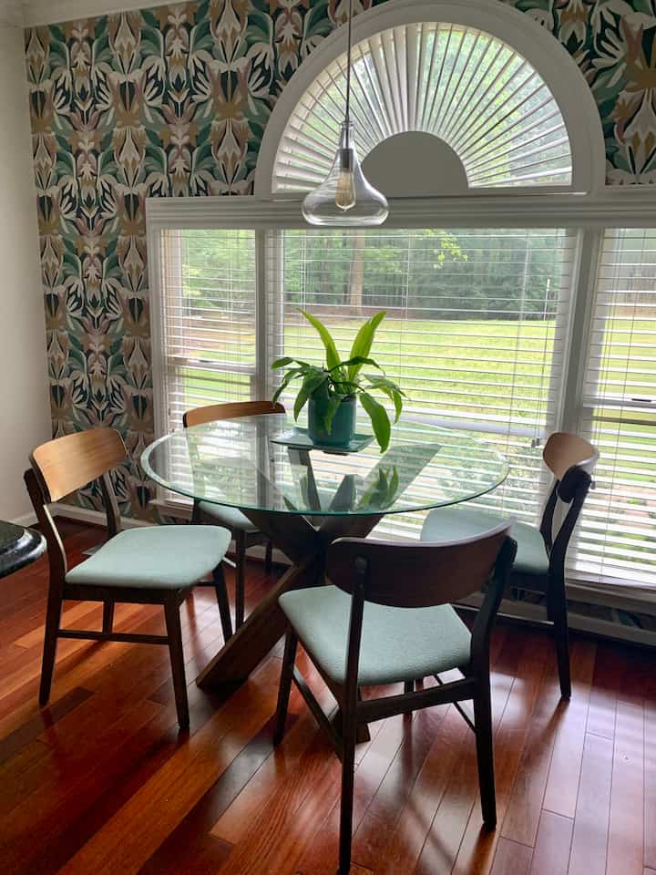 Wood tone and beige wallpapered 4-person dining room with glass dining table and pendant light in mid-century modern style