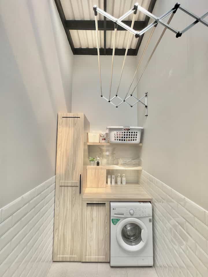 White and natural color toned narrow and long laundry room featuring custom cabinets and washing machine with neat atmosphere