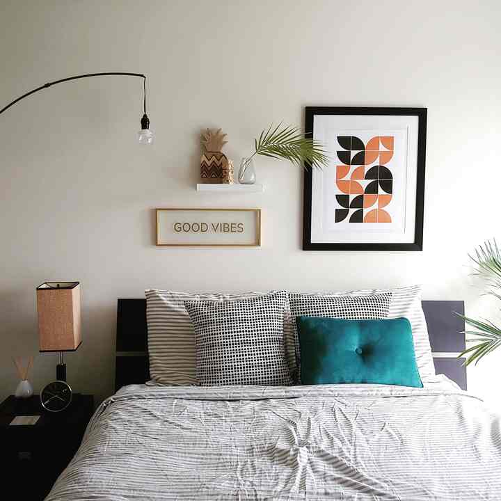 Light gray toned bedroom featuring a central bed with cushions, nightstand on left holding a clock and table lamp, showcasing a simple atmosphere