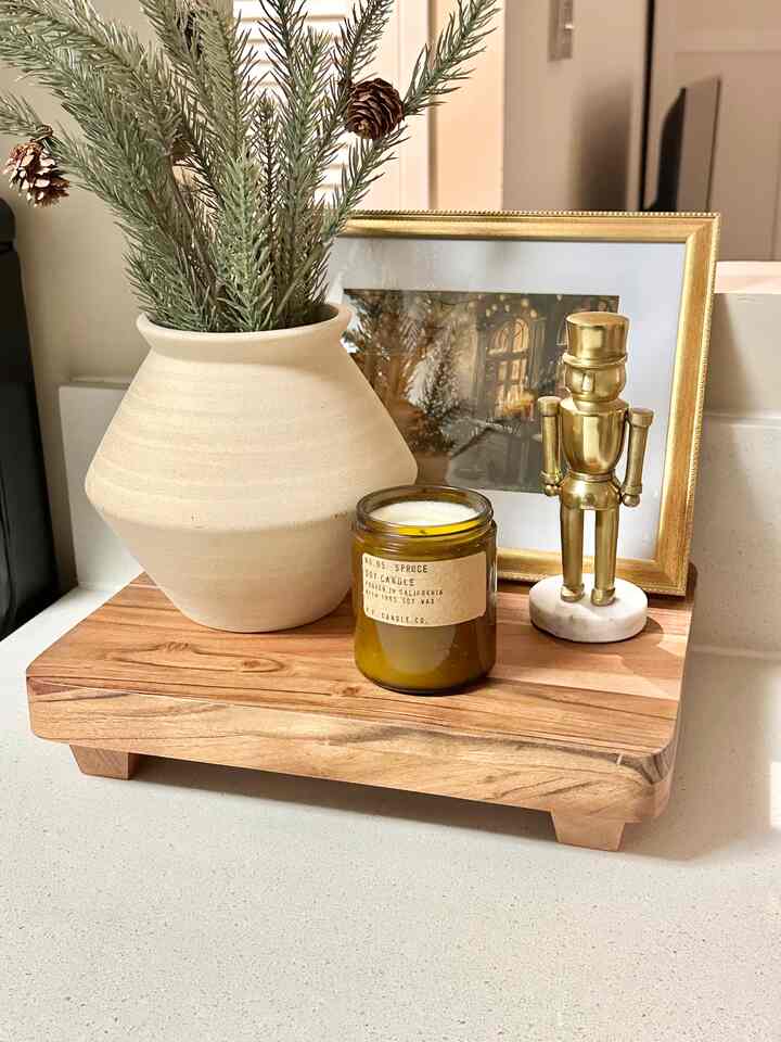 Kitchen space in gold and natural tones featuring a wooden tray holding a candle, a pot with spruce branches, and a gold nutcracker figurine with warm ambiance
