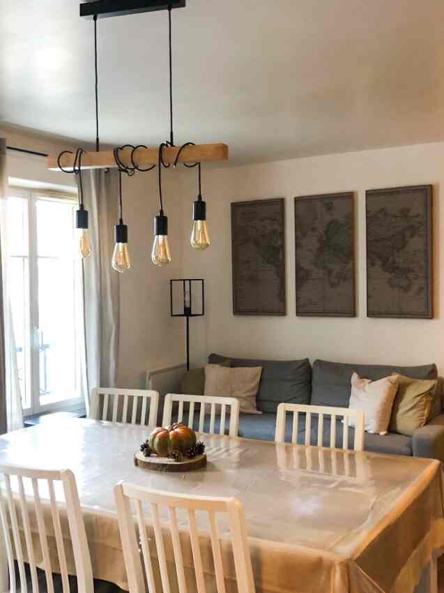 Light and dark gray toned living room featuring a central dining table with white chairs and a dark gray sofa bed on the right, creating a cozy atmosphere