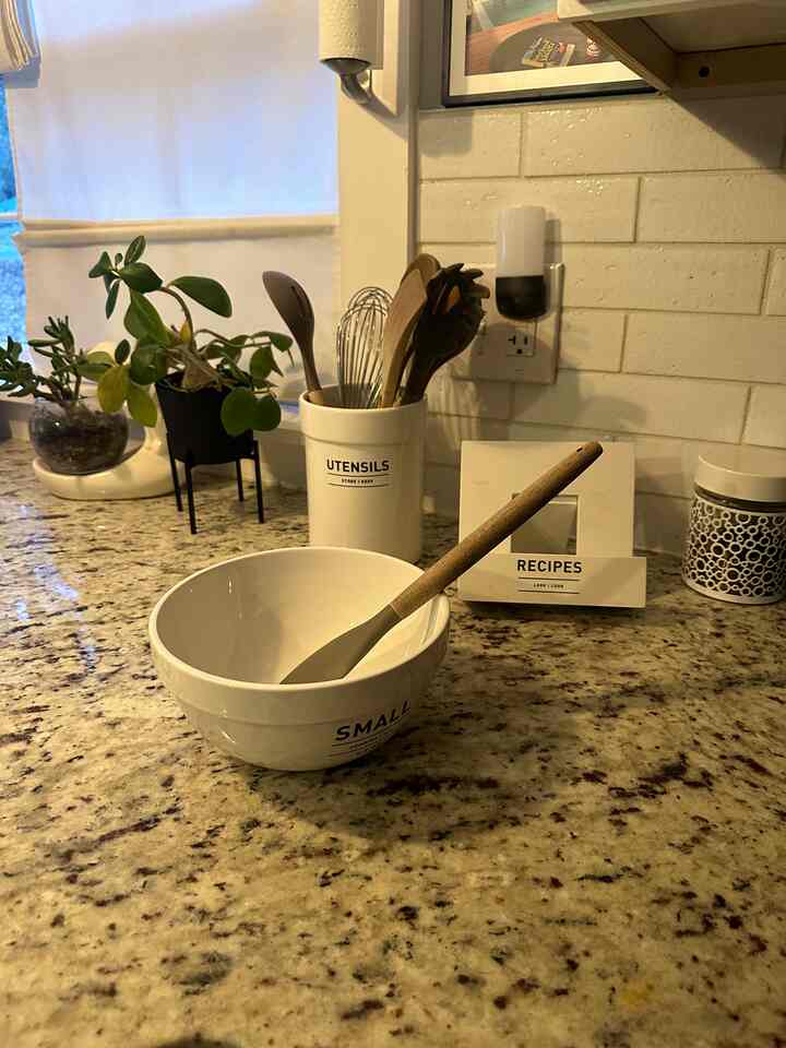 Modern kitchen with white and natural tones, featuring neatly arranged kitchen utensils and mixing bowls on a granite countertop