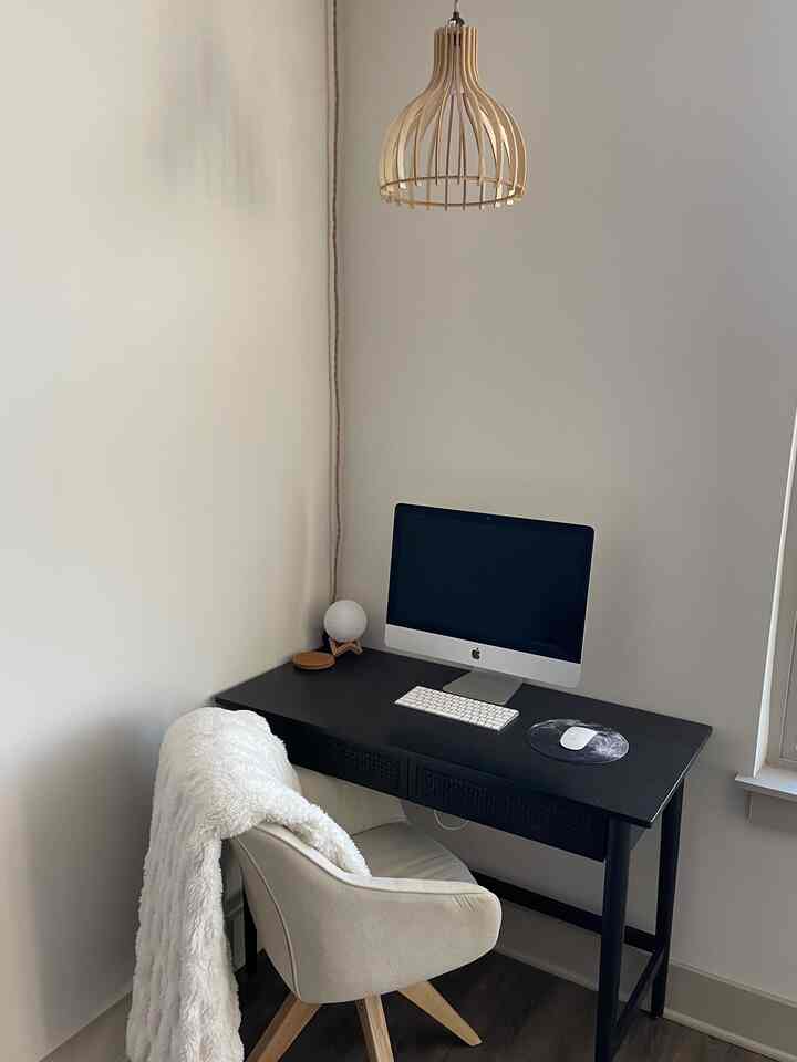 A clean single household home office in white, black, and wood tones featuring a desk, office chair, and pendant light creating a cozy atmosphere