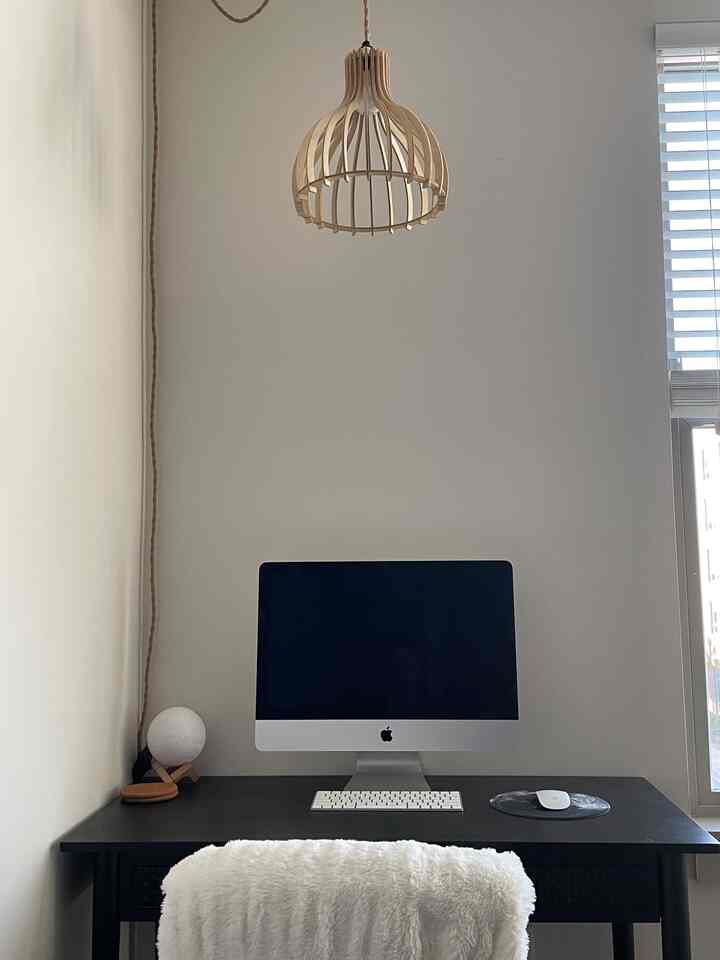 A compact, simple home office with white walls and a black desk, featuring a natural wood pendant light centrally placed