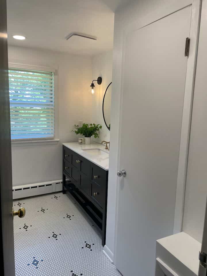 Scandinavian style bathroom in white and black tones featuring a black vanity, wall sconce, round mirror, and a plant with a sleek atmosphere