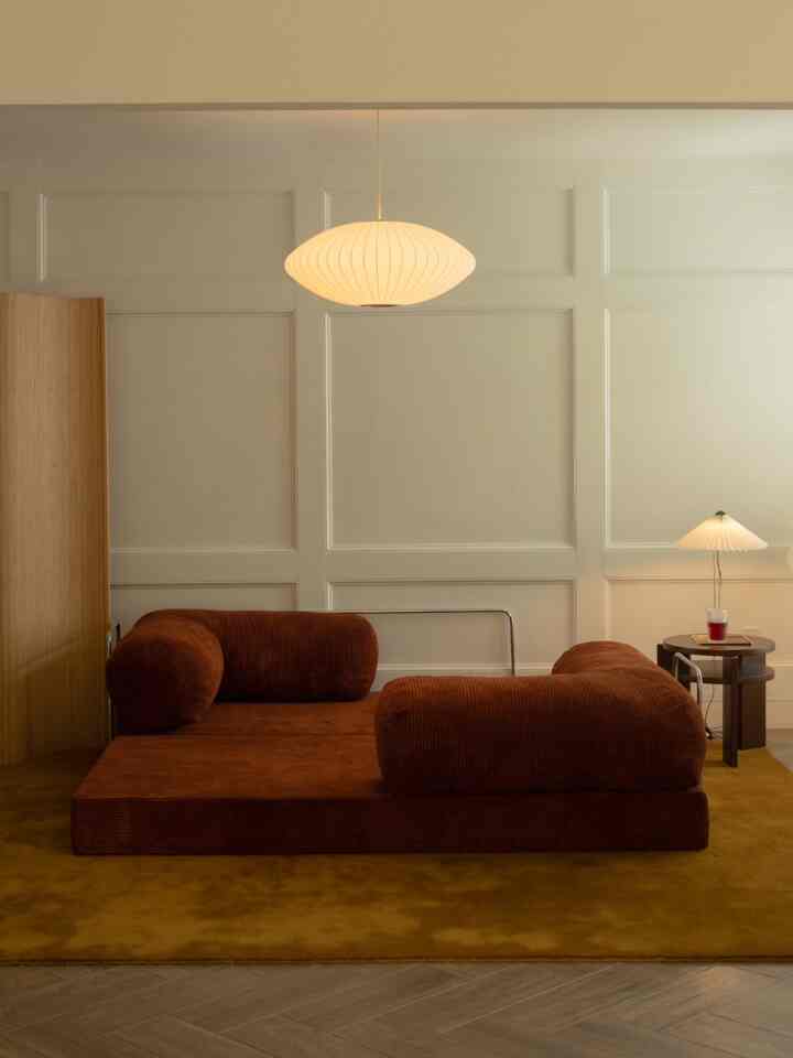 Warm natural toned living room featuring a brown sofa, golden mustard rug, pendant light, and bamboo room divider creating a cozy atmosphere